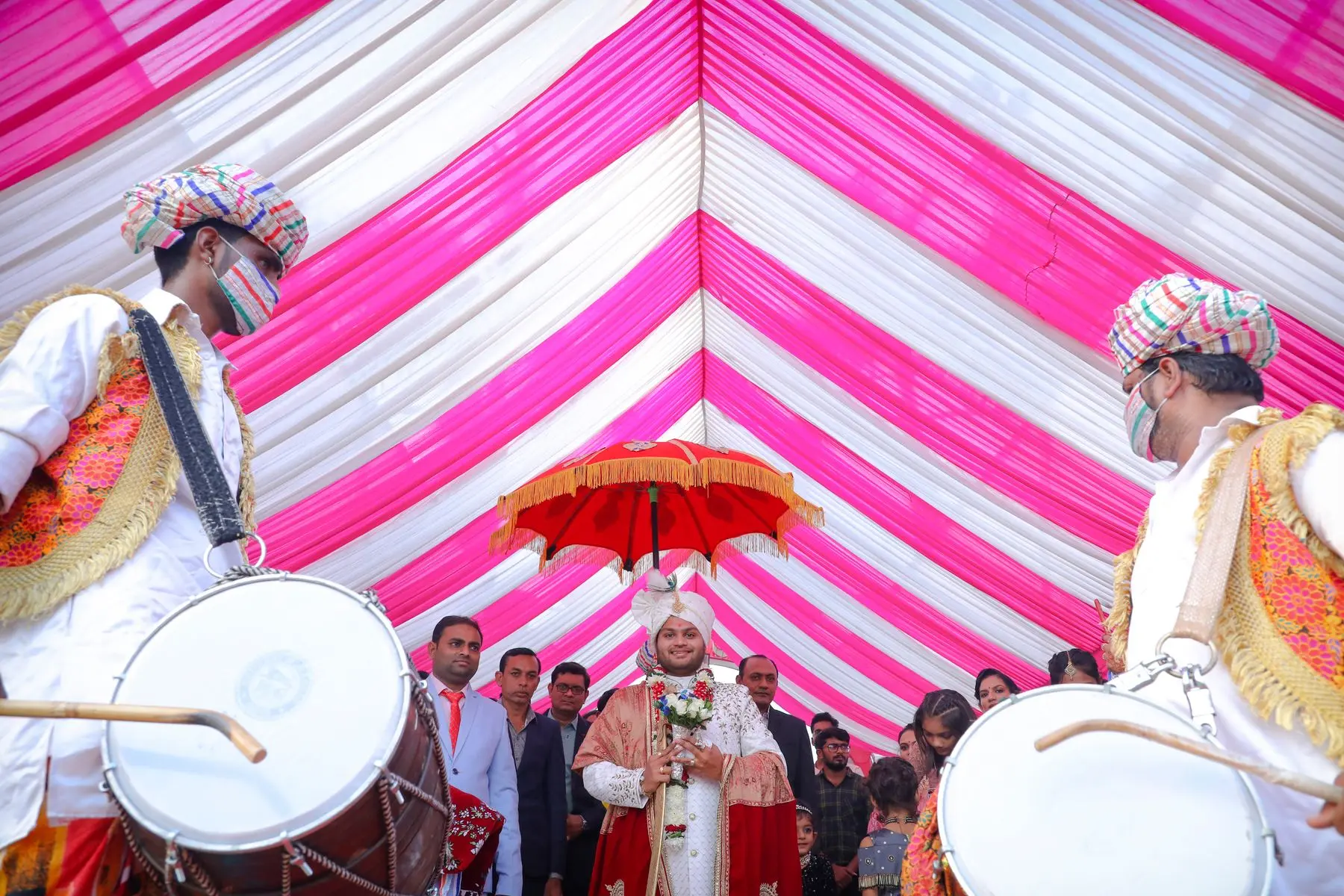 Wedding baraat procession moves beneath a colourful canopy as drummers lead the way