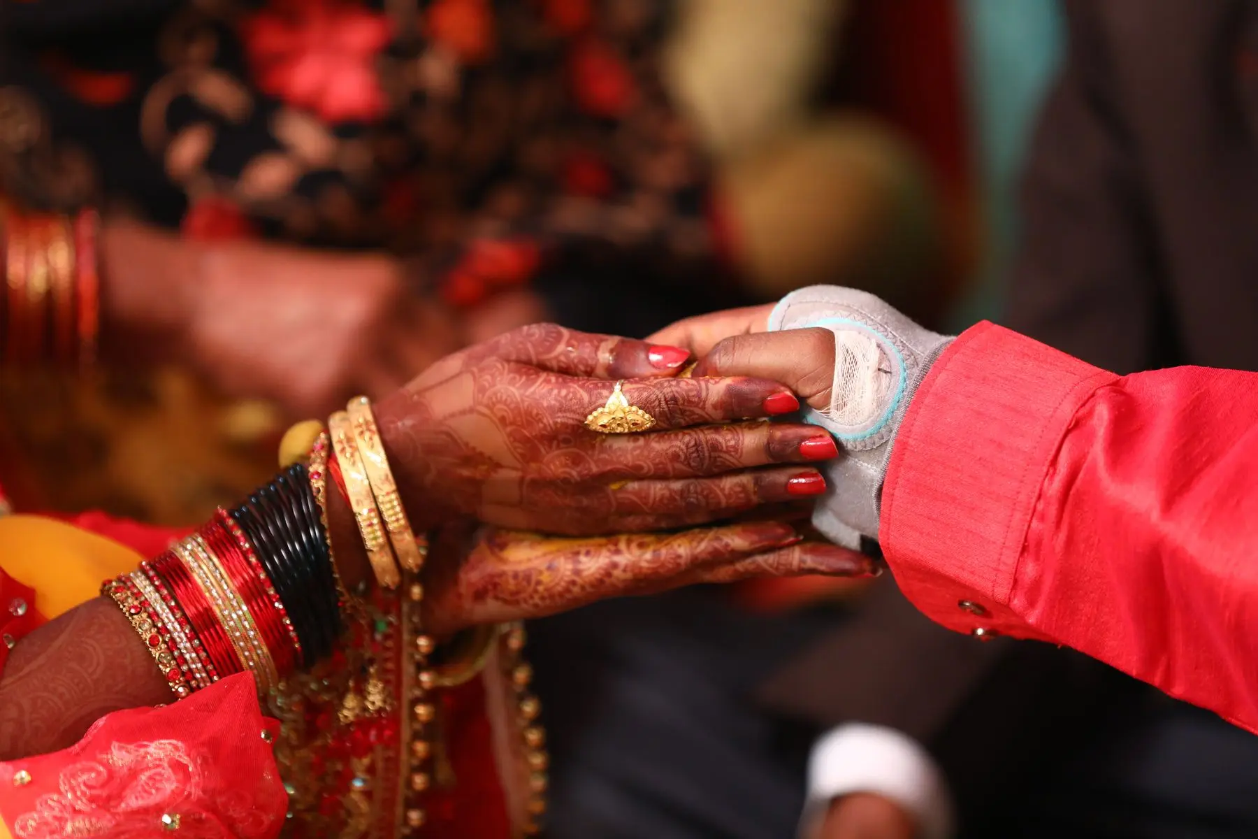 A couple’s hands meet during a wedding ceremony, with henna and traditional jewellery.