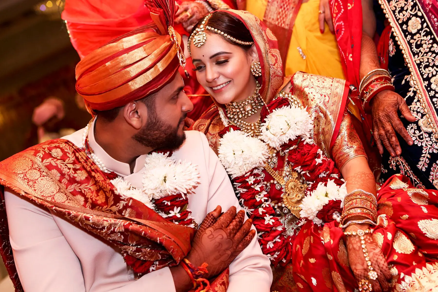 Indian bride and groom share a close, joyful moment in traditional red and gold wedding attire