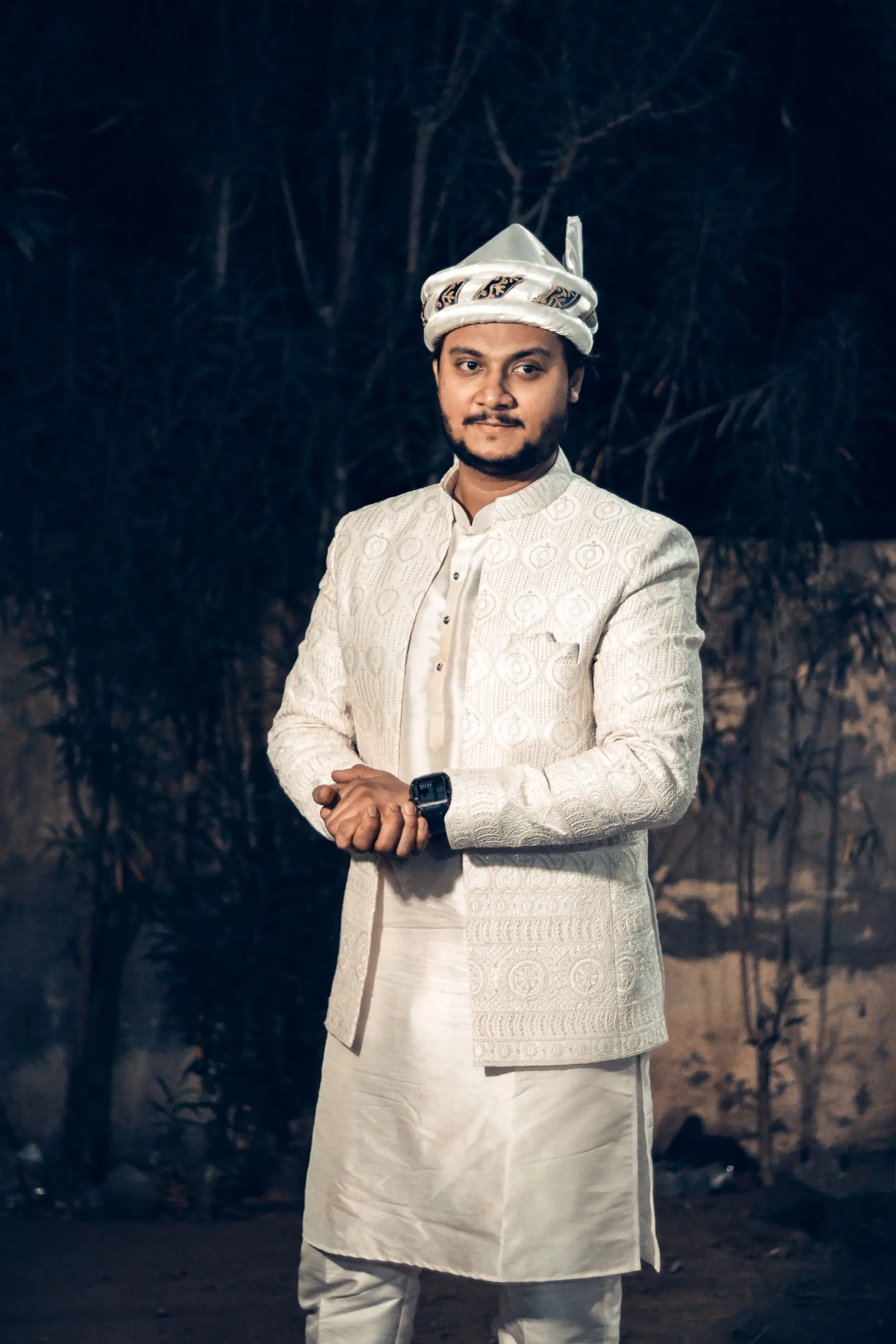 Indian groom in an ivory sherwani and traditional turban, photographed outdoors.