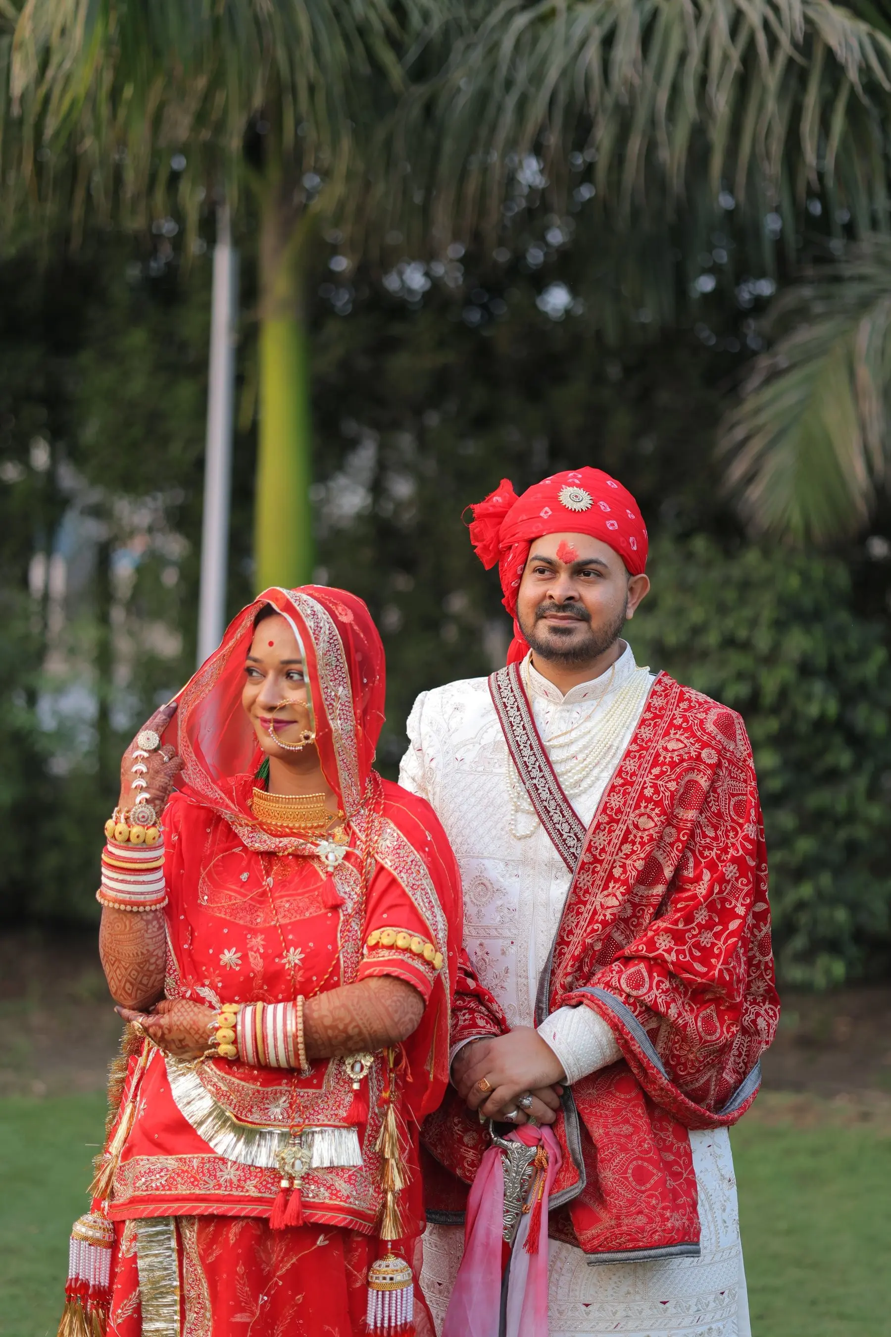 A couple pause together outdoors in evening light, dressed for a pre-wedding portrait.