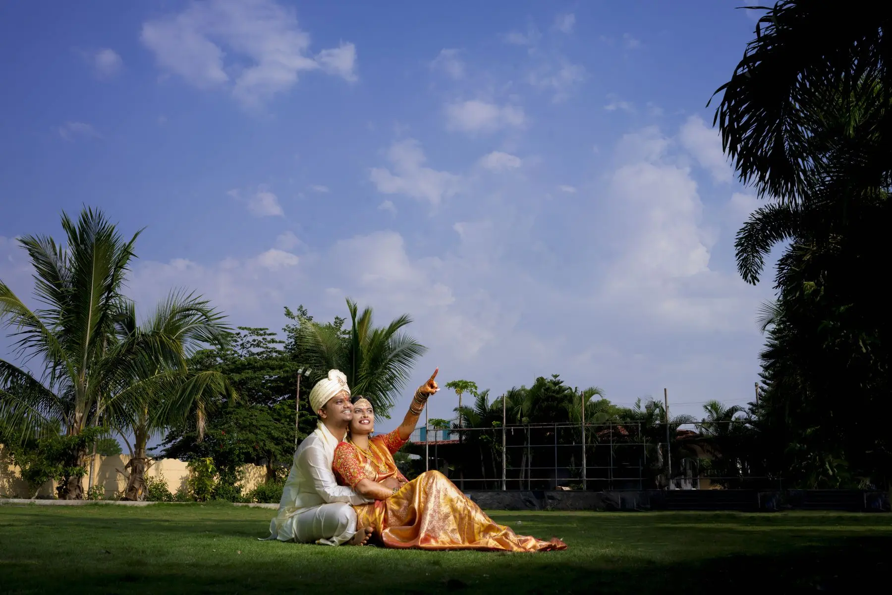 Indian couple in traditional wedding clothes photographed together in a wide garden landscape.
